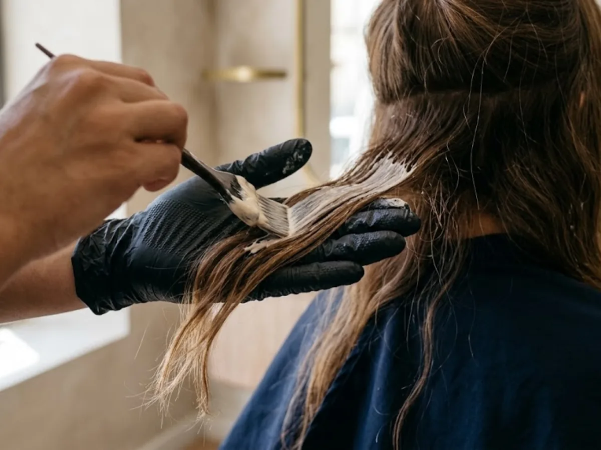Peluquera pintando aclarado a mano alzada sobre una sección de pelo castaño